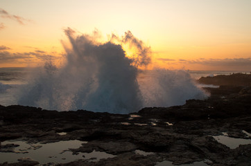 Waves spraying high over rocks at sunset