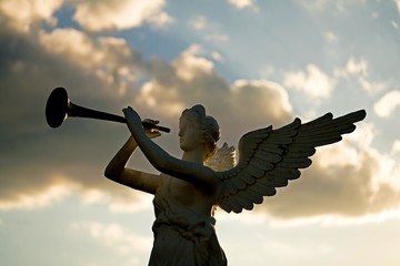 silhouette of angel blowing golden horn during sunrise against dramatic sky 