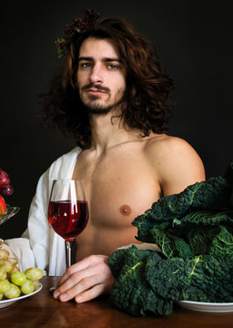 photo portrait of a half naked guy with long curly hair at the table with a glass of red wine and grapes