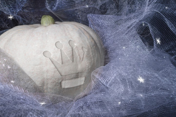 conceptual image of white pumpkin with crown symbol lying in sparkling tulle