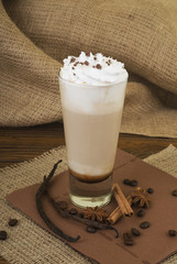 Coffee Latte. Coffee with whipped cream topping  in a tall glass on a wooden background with burlap