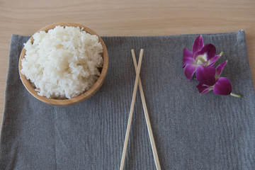 Cooked rice in a wooden bowl and chopsticks on a wood background.