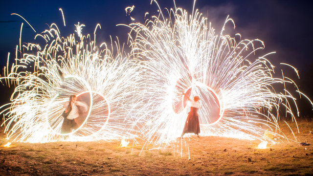 Amazing two performers Fire Show with a fireworks. Double O-shape full-round lines with a lot of sparks. And rapt admirative audience around. Beautiful wedding night in Carpathian mountains in Ukraine