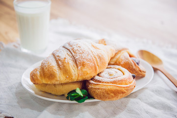 Close up continental breakfast with assortment of fresh pastries and glass of milk on the background. Selective focus