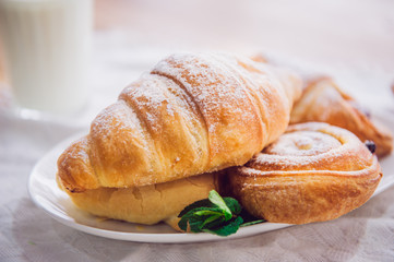 Close up continental breakfast with assortment of fresh pastries and glass of milk on the background. Selective focus