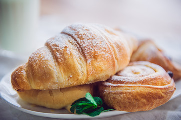 Close up continental breakfast with assortment of fresh pastries and glass of milk on the background. Selective focus
