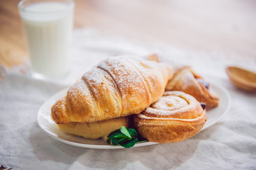 Close up continental breakfast with assortment of fresh pastries and glass of milk on the background. Selective focus