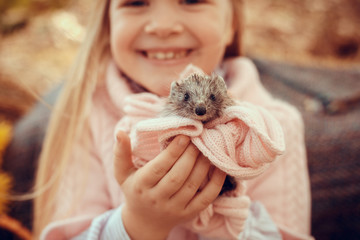 beautiful small girl with cute and funny hedgehog baby in autumn nature © Olena_Molchanova