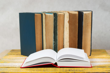 Open book, stack of hardback books on wooden table.