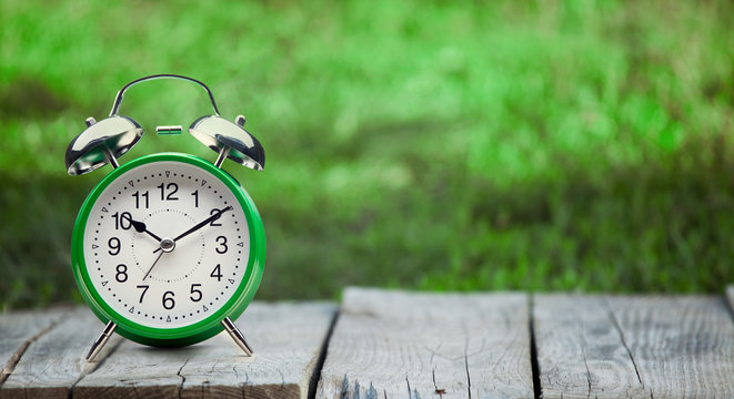 green clock on old wooden table in the summer garden on a sunny