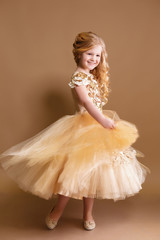 little girl like a doll with curly golden hair in nice gold dress © Olena_Molchanova