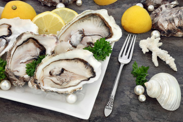 Oysters on ice with antique silver fork with lemon fruit, parsley herb, shells and pearls on a porcelain plate on marble. 