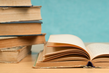 Open book, stack of hardback books on wooden table.