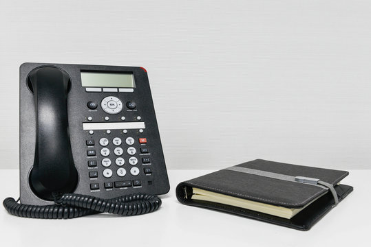 Black IP Phone and notebook on the white table