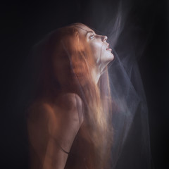Beautiful model with red hair posing behind a black fabric and a veil in a studio - 136698515