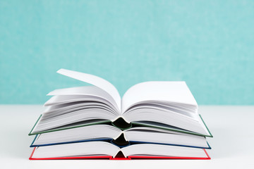 Open book, stack of hardback books on table.