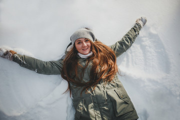 Fototapeta na wymiar Beautiful joyful young woman laying down on snow moving her arms