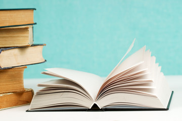 Open book, stack of hardback books on table.