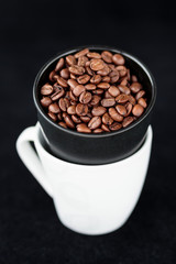 Coffee beans in coffee mug on black background