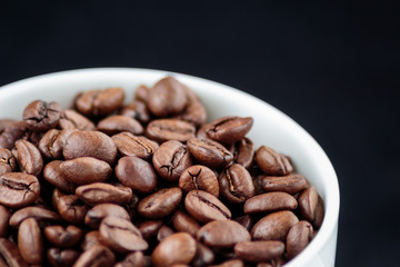 Coffee beans in coffee mug on black background close up
