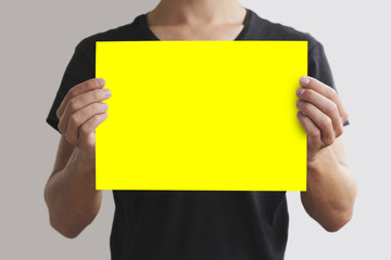 Man in black t shirt holding blank yellow A4 paper horizontally.