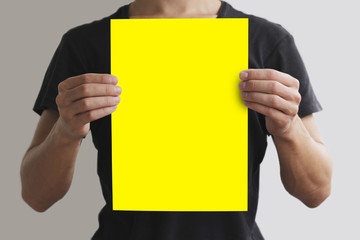 Man in black t shirt holding blank yellow A4 paper vertically. L