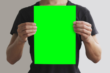 Man in black t shirt holding blank green A4 paper vertically. Le