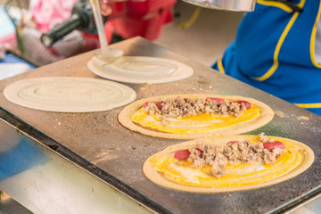 cooking scene of Thai Crepes with minced pork on the stove - It name is KANOM TOKYO dessert sweets in Thailand ; thin flat pancake filled with pork or sausage. It is a Thai street snack 