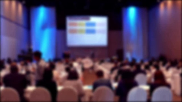 People sit on rows of chairs in large conference convention hall during meeting seminar, defocused blur background

