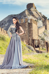 Fototapeta premium Summer outdoors portrait of beautiful furious scandinavian warrior ginger woman in grey dress with metal chain mail. Fortress Sudak, Crimea