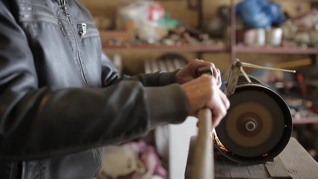 Old man sharpening his ax on a grinder in an workshop