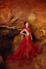 Fototapeta na wymiar dynamic fashion shot. sexy woman in red dress, Gothic fairy shooting in a dark cave. Red cavern, Crimea