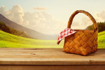 Picnic basket with checked tablecloth on wooden table over beautiful landscape background
