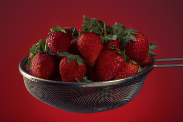 Fresh strawberries in a colander on a red background