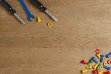 Kids construction toys tools: colorful screwdrivers, screws and nuts on wooden background. Top view. Flat lay. Copy space for text