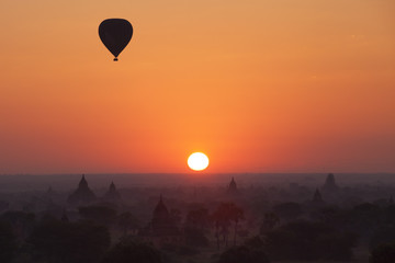 Orange sunrise in Bagan with balloon and foggy temples 