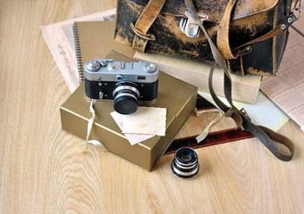 Old camera, film, lens and vintage satchel on wooden background.