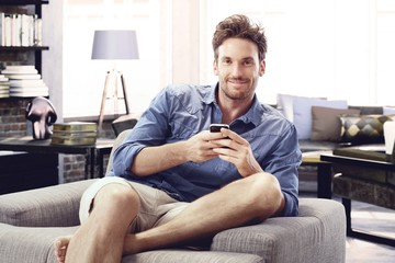 Happy man at home sitting using mobile phone