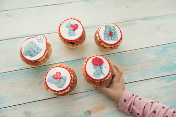 Five cupcakes Teddy bear with hearts and flowers on a blue wooden background. Takes in hand