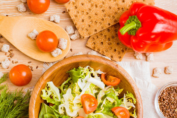 Смесь листьев салатов радичио, фриссе, лолло россо в деревянной тарелке, помидоры черри, перец, ржаные хлебцы и отруби