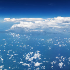 Clear blue sky. Aerial view from passenger cabin through plane window. Aircraft fly in mid air. Flight above earth and beautiful white cloud. Vacation tour, travel background with copy space