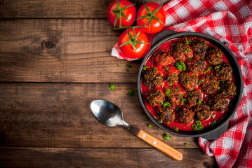 Homemade meatballs from minced beef in tomato sauce with fresh herbs in a frying pan on a wooden table. top view, copy space