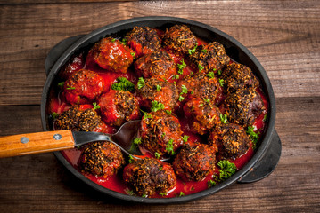 Homemade meatballs from minced beef in tomato sauce with fresh herbs in a frying pan on a wooden table. close view, copy space