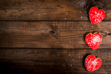 Background for Valentine's Day: a wooden table, and three biscuits in shape of hearts with red icing, top view, copy space