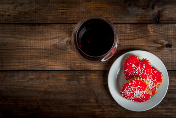 Background for Valentine's Day: glass with wine and three biscuits in shape of hearts with red icing, top view, copy space