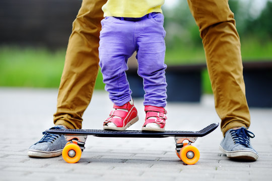 Toddler girl learning to skateboard with her father close up