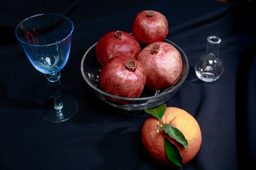 Apfelsine und Granatapfel mit blauem Weinglas und kleiner Vase
