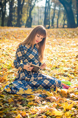 beautiful girl with long straight hair in a blue long dress reading a book in the autumn park