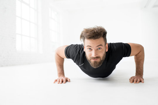 Handsome man in the black sportswear making pushups indoors in the white gym interior