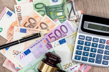 different euros bills, hammer, calculator and pen on desk.